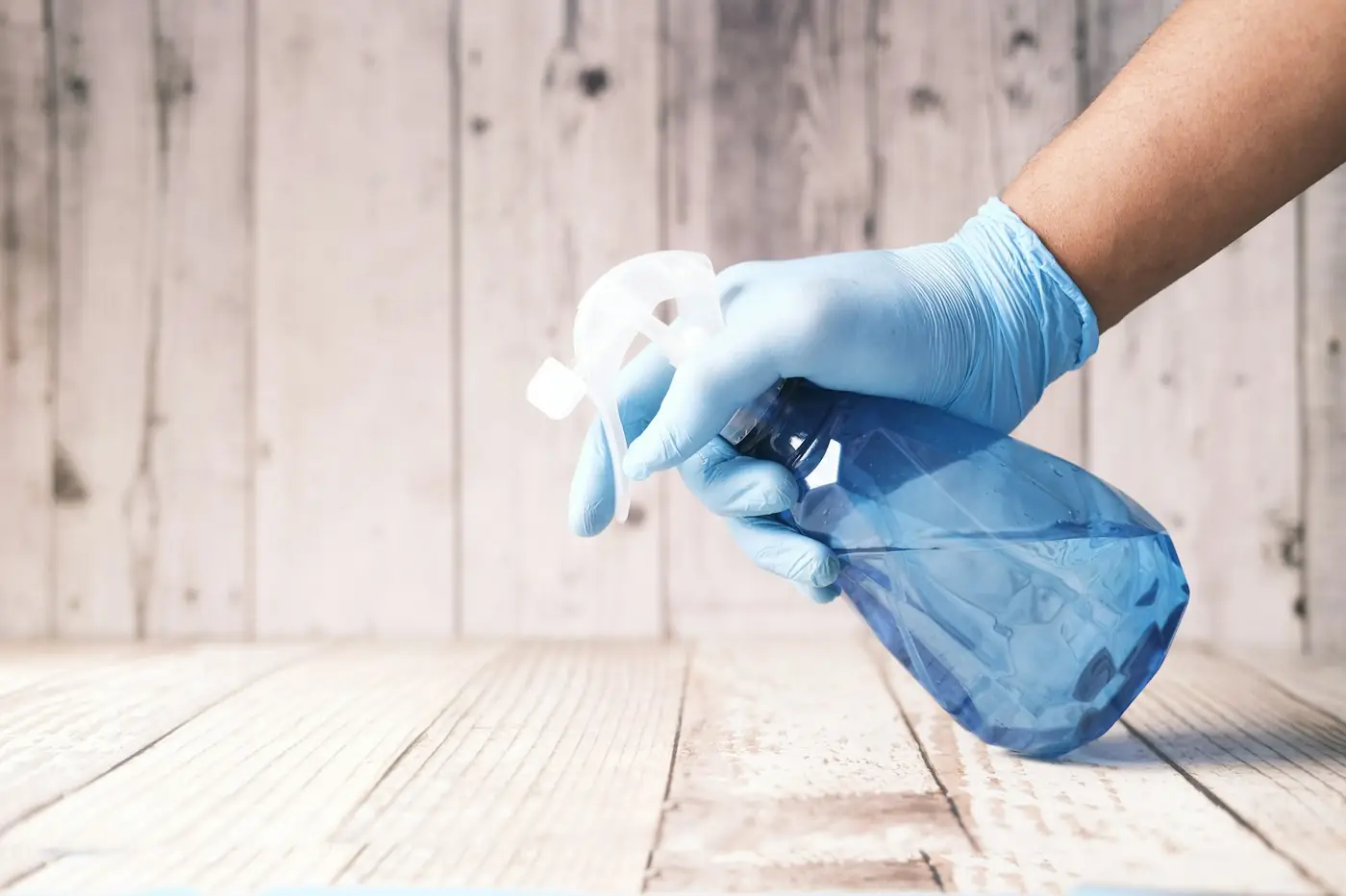 Hand in blauem Handschuh mit Sprühflasche